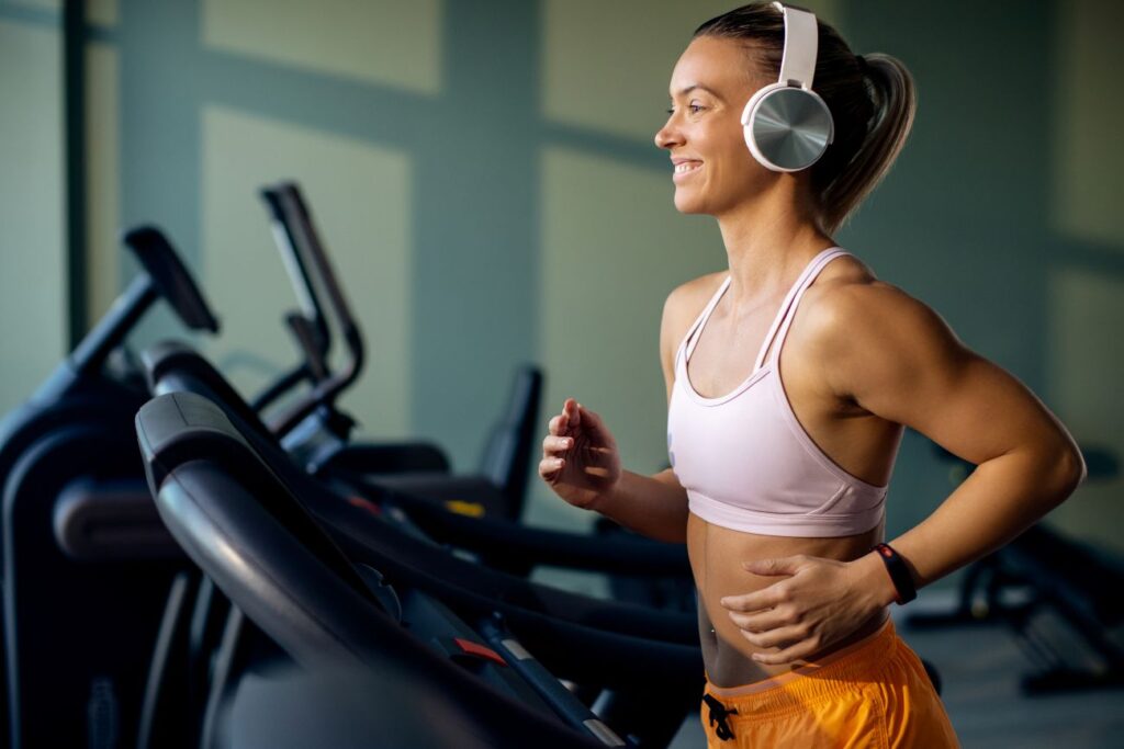Mulher correndo e ouvindo música na esteira mostra como a trilha sonora certa melhora foco e desempenho no treino físico.
