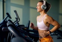 Mulher correndo e ouvindo música na esteira mostra como a trilha sonora certa melhora foco e desempenho no treino físico.