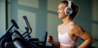 Mulher correndo e ouvindo música na esteira mostra como a trilha sonora certa melhora foco e desempenho no treino físico.
