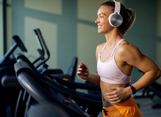 Mulher correndo e ouvindo música na esteira mostra como a trilha sonora certa melhora foco e desempenho no treino físico.