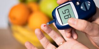 Pessoa medindo a glicose no sangue com glicosímetro, mostrando resultado de 95 mg/dL, com frutas desfocadas ao fundo.
