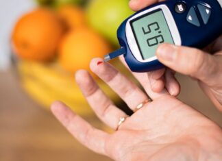 Pessoa medindo a glicose no sangue com glicosímetro, mostrando resultado de 95 mg/dL, com frutas desfocadas ao fundo.