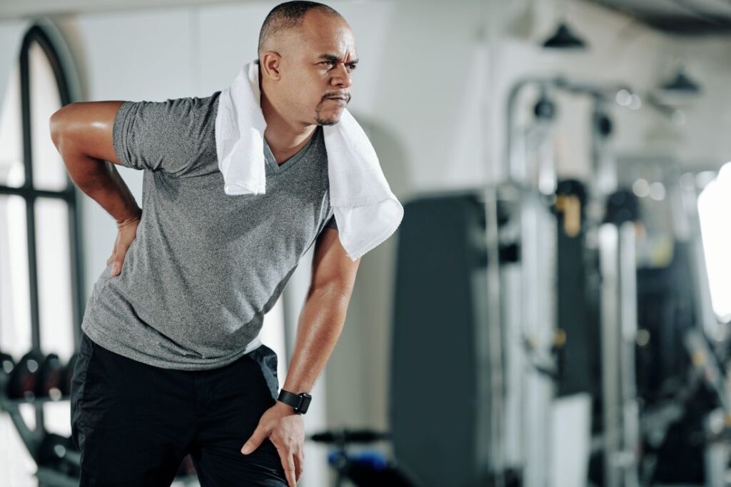 Homem jovem com dor na lombar e joelho Homem jovem com dor na lombar e joelho, ilustrando desconforto comum por má postura ou fraqueza muscular.
