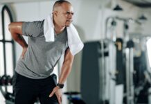 Homem jovem com dor na lombar e joelho, ilustrando desconforto comum por má postura ou fraqueza muscular.
