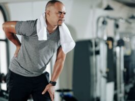 Homem jovem com dor na lombar e joelho, ilustrando desconforto comum por má postura ou fraqueza muscular.
