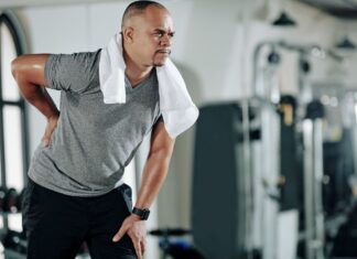 Homem jovem com dor na lombar e joelho, ilustrando desconforto comum por má postura ou fraqueza muscular.