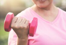 Pessoa usando camiseta rosa segura um halter rosa durante exercício ao ar livre, em imagem associada à atividade física e à prevenção do câncer de mama.