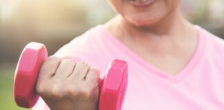 Pessoa usando camiseta rosa segura um halter rosa durante exercício ao ar livre, em imagem associada à atividade física e à prevenção do câncer de mama.