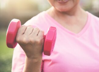 Pessoa usando camiseta rosa segura um halter rosa durante exercício ao ar livre, em imagem associada à atividade física e à prevenção do câncer de mama.
