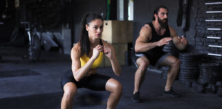 Casal fitness executando agachamentos em academia moderna, demonstrando um dos exercícios mais eficazes para quem busca como engrossar as pernas.
