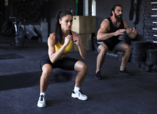 Pernas finas nunca mais: descubra como engrossar as pernas com treinos simples Casal fitness executando agachamentos em academia moderna, demonstrando um dos exercícios mais eficazes para quem busca como engrossar as pernas.