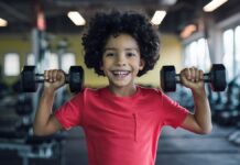 Musculação para crianças e adolescentes: saiba quando começar Pequeno atleta simula treino de musculação para crianças e adolescentes, segurando halteres com as mãos.
