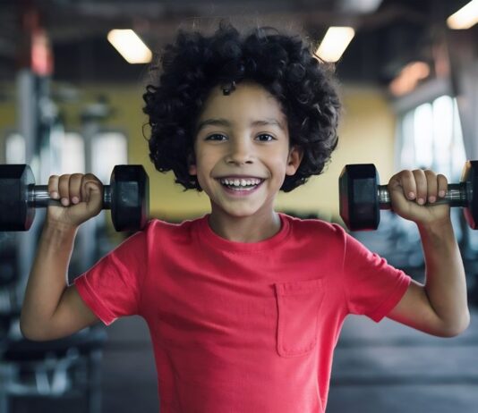 Musculação para crianças e adolescentes: saiba quando começar Pequeno atleta simula treino de musculação para crianças e adolescentes, segurando halteres com as mãos.