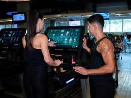 Cardio: Antes ou depois da musculação? Mulher apertando botão de iniciar na esteira com professor da academia ao lado.