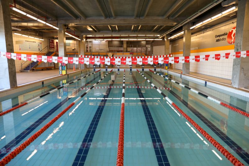 Piscina coberta da Cia Athletica, com raias demarcadas por boias vermelhas, pretas e brancas, prontas para treinos de natação.