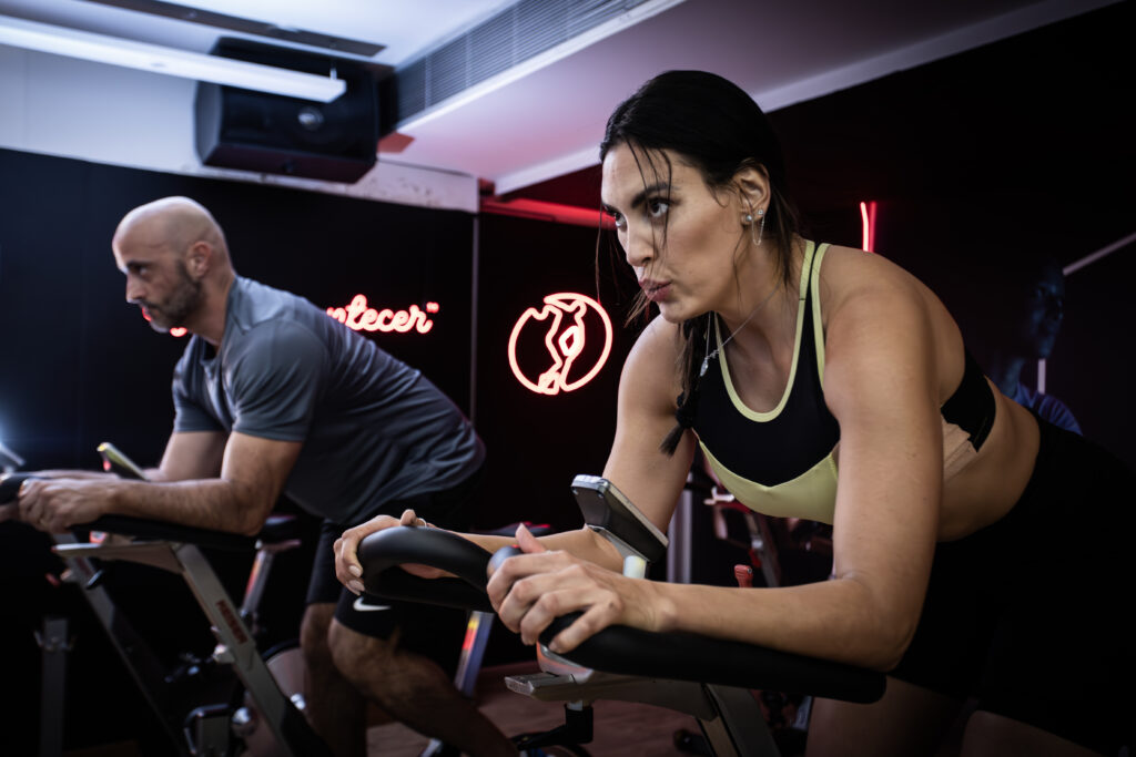 Duas pessoas realizam exercícios em bicicletas de spinning durante um treino na Cia Athletica.