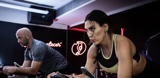 Duas pessoas realizam exercícios em bicicletas de spinning durante um treino na Cia Athletica.