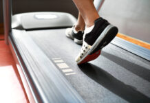 Esteira emagrece? Saiba como caminhada e corrida ajudam na perda de gordura Pessoa caminhando em uma esteira durante treino cardiovascular, com foco nos pés em movimento sobre a lona do equipamento, ilustrando caminhada e corrida como estratégias para emagrecimento e melhora do condicionamento físico.