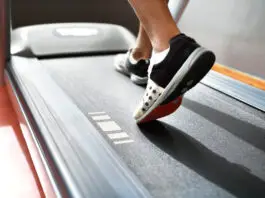 Pessoa caminhando em uma esteira durante treino cardiovascular, com foco nos pés em movimento sobre a lona do equipamento, ilustrando caminhada e corrida como estratégias para emagrecimento e melhora do condicionamento físico.