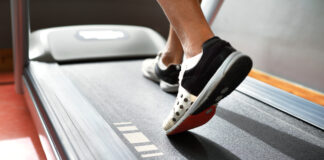 Pessoa caminhando em uma esteira durante treino cardiovascular, com foco nos pés em movimento sobre a lona do equipamento, ilustrando caminhada e corrida como estratégias para emagrecimento e melhora do condicionamento físico.