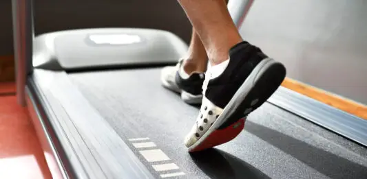 Pessoa caminhando em uma esteira durante treino cardiovascular, com foco nos pés em movimento sobre a lona do equipamento, ilustrando caminhada e corrida como estratégias para emagrecimento e melhora do condicionamento físico.