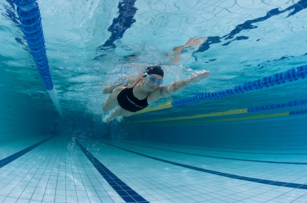 Você já considerou fazer aula de natação? Além de ser uma atividade revigorante, também é um excelente exercício físico para colocar a saúde em dia.
Além disso, a prática é indicada para todos os tipos de pessoas de todas as idades, por conta dos efeitos que a água proporciona para o corpo. Então, quer saber mais sobre natação? Acompanhe este conteúdo!
Orientações sobre natação
Para receber um plano de aula de natação, em primeiro lugar, você precisará passar por uma avaliação com o professor, e também deve realizar um exame médico.
Apesar da natação ser uma atividade de baixo impacto, algumas pessoas devem tomar cuidado. Por exemplo, pessoas que têm alergias de pele podem ficar com a pele mais irritada, por causa dos produtos que colocam para a limpeza da piscina.
Quem também sofre de graves problemas na coluna, deve procurar outra atividade física. Isso porque a prática exige muita força dos músculos posteriores.
Pessoas que têm alguma infecção pulmonar, como bronquite, ou problemas respiratórios, como sinusite, podem ter alguma dificuldade para acompanhar a aula. Por isso, é essencial que tenha autorização do seu médico.
Como é uma aula de natação?
Antes e depois das aulas, é ideal que você realize alongamentos para aquecer o corpo, mas, dentro d’água. Isso vai aumentar o fluxo sanguíneo que vai para os músculos e lubrificar as articulações. 
Portanto, você deve nadar de forma suave, por uns 10 minutos, e realizar exercícios de alongamento.
Enfim, a aula de natação para iniciantes é uma excelente forma de começar a praticar a atividade física. Se você ainda não sabe nadar, ou se não conhece as técnicas de nado, vai aprender isso nas aulas, conforme for subindo de nível de classe.
Mas, se você já sabe nadar e conhece as técnicas, pode fazer aula para aprimorar suas habilidades.
Além disso, você pode realizar aulas livres, apenas para praticar o que já aprendeu. Na Cia Athletica, chamamos de Natação Flex Time. Essa modalidade permite que você nada a qualquer hora do dia, em qualquer dia da semana.
Também não precisa fazer esta aula com outros alunos, pode nadar sozinho na raia. Contudo, você ainda terá o acompanhamento de um professor, para qualquer dúvida que tiver.
