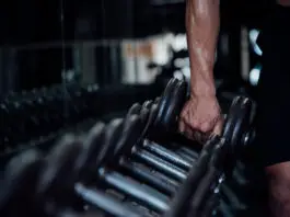 Musculação emagrece e talvez mais do que o cardio em alguns casos Pessoa segurando um halter em academia durante treino de musculação, com foco no braço e nos pesos em ambiente escuro e moderno.