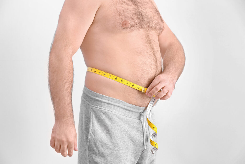Perder barriga: o que realmente funciona para diminuir gordura abdominal Homem adulto mede a circunferência da barriga com fita métrica, evidenciando gordura abdominal.
