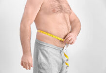 Homem adulto mede a circunferência da barriga com fita métrica, evidenciando gordura abdominal.