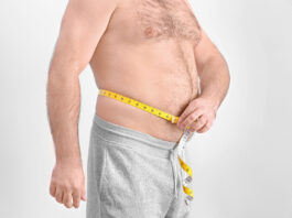 Homem adulto mede a circunferência da barriga com fita métrica, evidenciando gordura abdominal.