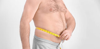 Homem adulto mede a circunferência da barriga com fita métrica, evidenciando gordura abdominal.