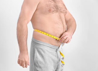 Homem adulto mede a circunferência da barriga com fita métrica, evidenciando gordura abdominal.