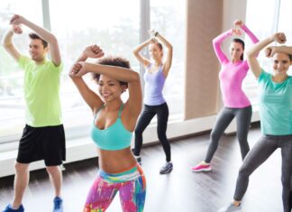 Para você que busca por opções de atividades físicas para queimar calorias, a aula de ritmos é uma excelente maneira de se movimentar, de aprender a dançar e até mesmo de fugir um pouco dos treinos aeróbicos convencionais. Aliás, essa modalidade de exercício tem se tornado muito popular nas academias, porque, além de oferecer muitos benefícios para os seus praticantes, ainda é uma atividade completa e muito divertida. Afinal, o que é aula de ritmos na academia? Neste post, vamos abordar como funciona essa categoria de esporte e quais são suas vantagens para os alunos. Acompanhe! O que é aula de ritmos? A aula de ritmo é uma atividade física aeróbica, que tem como princípio vários ritmos de dança. Nas aulas, acontece uma mistura de coreografias de níveis: fácil, médio e difícil, que devem ir aumentando conforme a intensidade de cada música. Além disso, essa prática é realizada de forma alegre e divertida, promovendo muitas queimas de calorias.