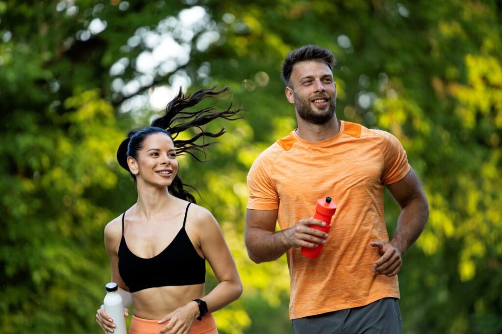 Casal jovem corre em parque arborizado durante o dia.