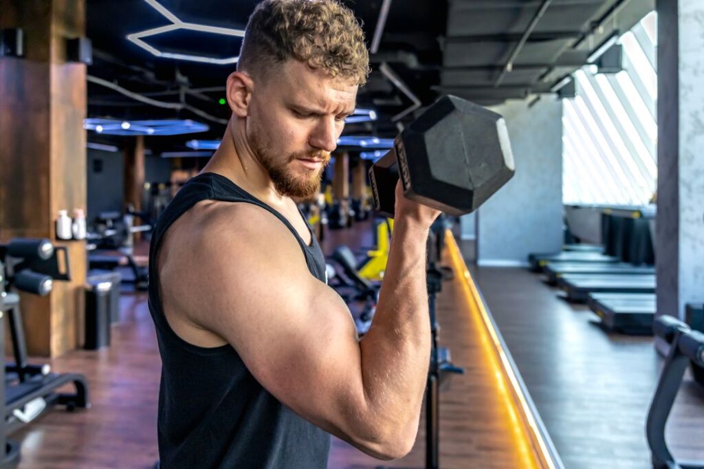 Homem em academia faz flexão de bíceps.