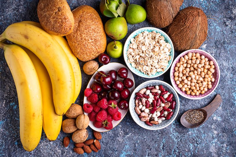 Uma variedade de alimentos à mesa, como frutas e grãos, que são alimentos ricos em fibras, fazem bem à saúde junto com os exercícios físicos
