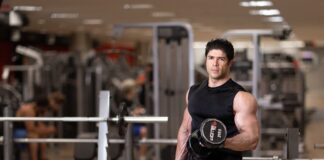 Homem musculoso segura peso para fazer exercícios de braço na academia