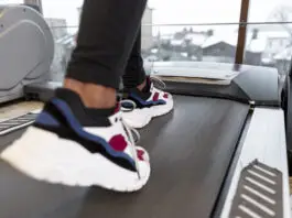 20 minutos de esteira todo dia emagrece? Veja o que influencia o resultado Close das pernas e dos pés de uma pessoa caminhando ou correndo em uma esteira, usando calça esportiva preta e tênis brancos com detalhes coloridos, em uma academia iluminada por grandes janelas.
