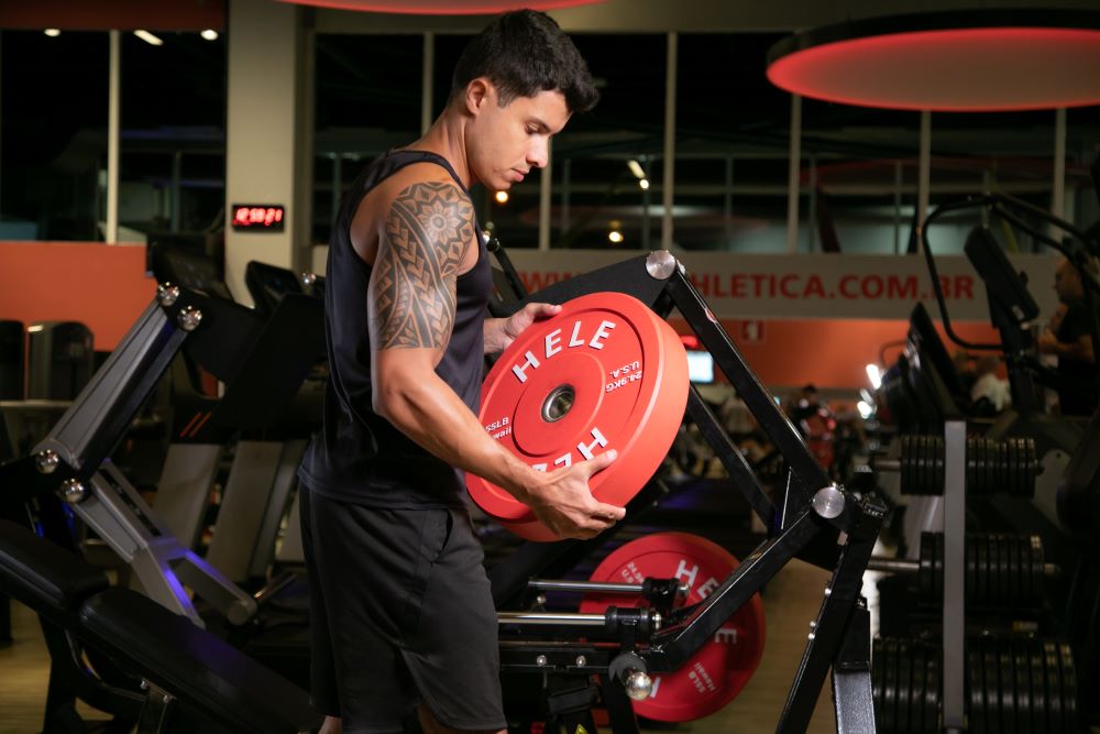 Homem colocando anilha em aparelho de leg press.