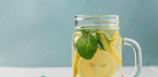 Fita métrica em mesa ao lado de jarra com água, hortelã e limão para emagrecimento