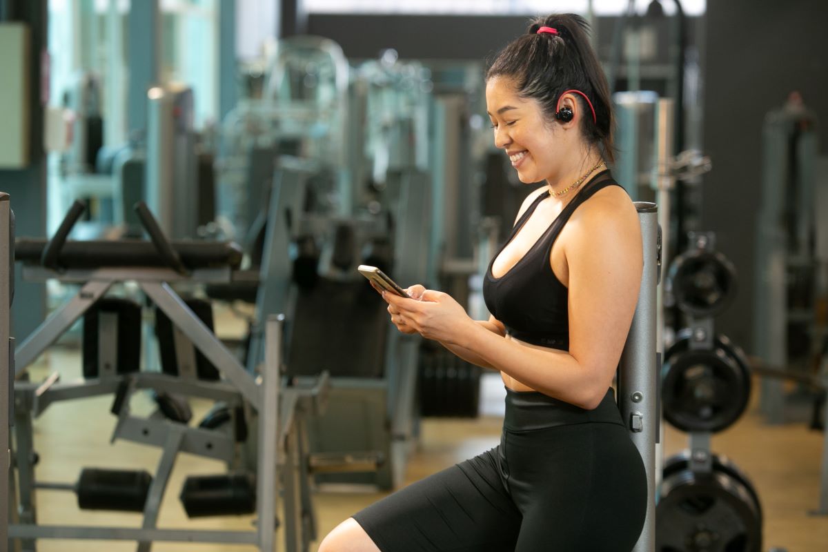 Mulher observa celular na academia, onde faz exercícios para ter longevidade com saúde