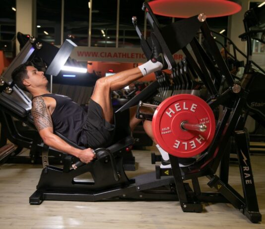 Homem em academia faz exercício de perna em aparelho Leg 45