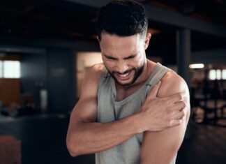 Homem na academia faz expressão de desconforto ao sentir dor no ombro