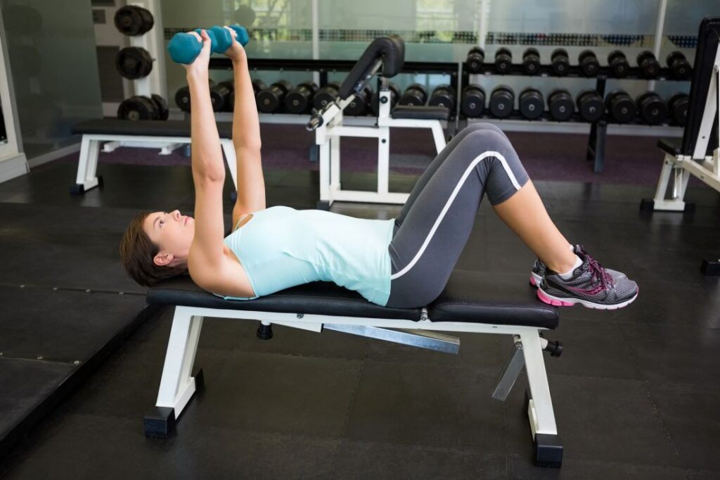 Mulher levantando halteres no exercício supino reto com halteres.