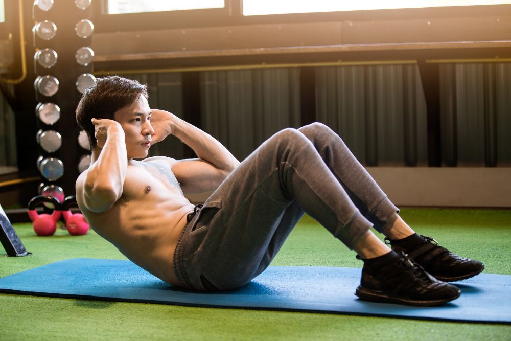 Homem sem camisa flexionando tronco e pernas em abdominal supra.