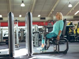 Mulher idosa sentada em aparelho de academia para realizar exercício na cadeira adutora.