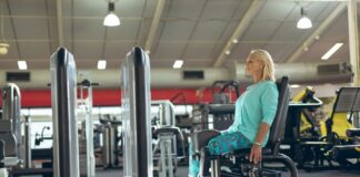 Mulher idosa sentada em aparelho de academia para realizar exercício na cadeira adutora.