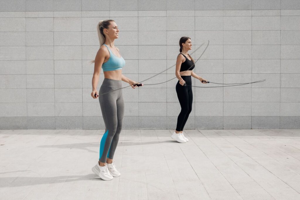 Mulheres com roupa de ginástica pulando corda em espaço de concreto.