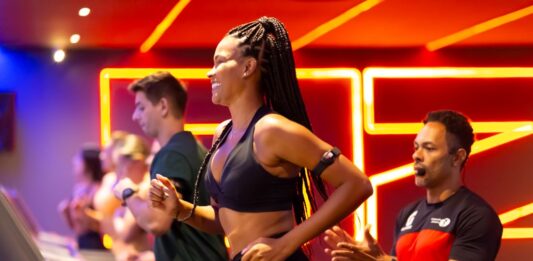 Mulher correndo na esteira com acompanhamento de professor em academia durante treino para iniciantes.