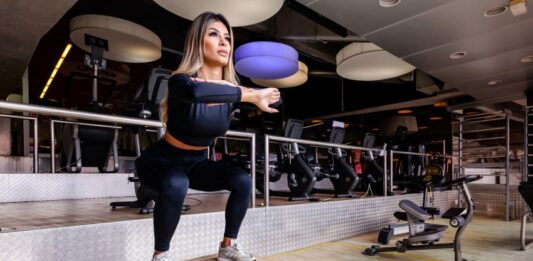 Mulher realizando agachamento em cima de caixa.